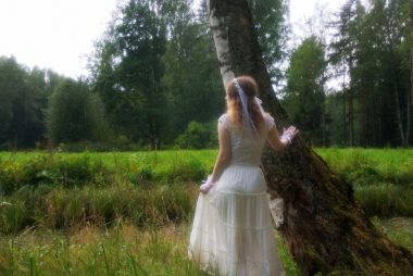 Woman in white dress stands in grassy field.